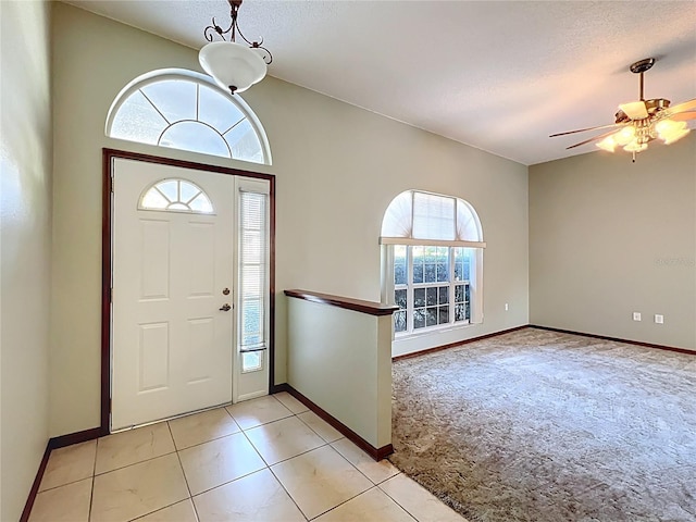 entryway featuring ceiling fan, light tile patterned floors, light colored carpet, and a textured ceiling