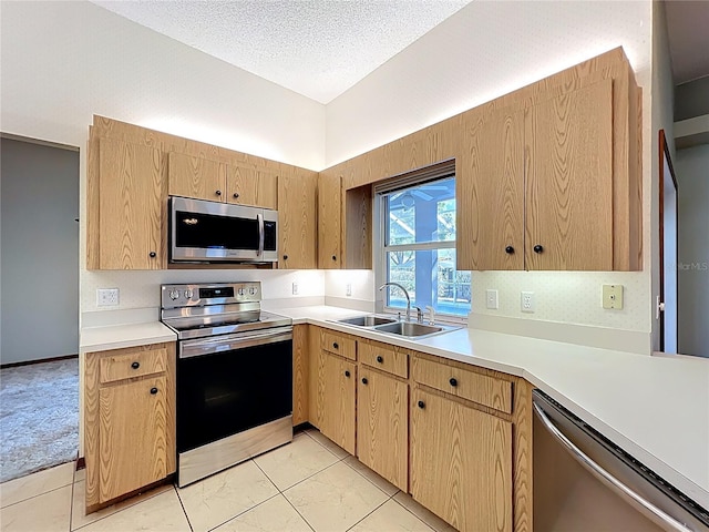 kitchen with light brown cabinetry, a sink, a textured ceiling, appliances with stainless steel finishes, and light countertops