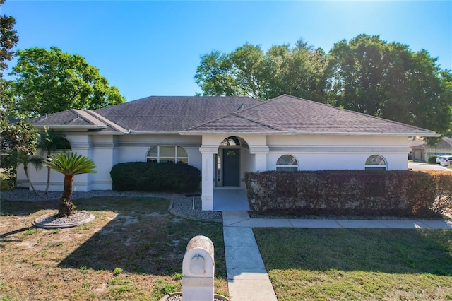 single story home with stucco siding, roof with shingles, and a front lawn