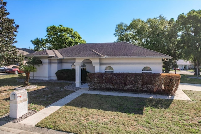 ranch-style house with stucco siding, a front yard, and a shingled roof