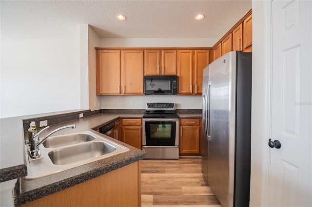 kitchen with dark countertops, light wood-type flooring, appliances with stainless steel finishes, a textured ceiling, and a sink