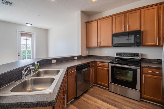 kitchen with dark countertops, visible vents, appliances with stainless steel finishes, wood finished floors, and a sink