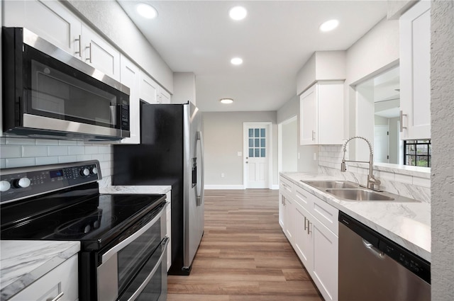 kitchen with a sink, tasteful backsplash, light wood-style floors, appliances with stainless steel finishes, and white cabinets