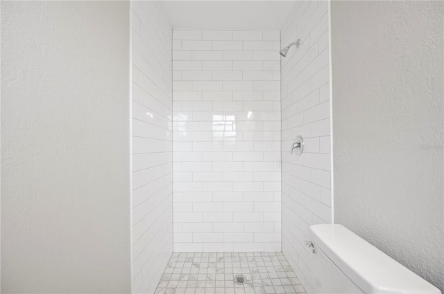 full bathroom featuring toilet, tiled shower, and a textured wall