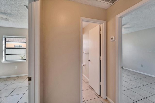 hallway featuring light tile patterned floors, a textured ceiling, and baseboards