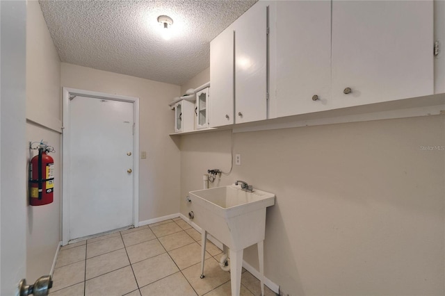 washroom with baseboards, light tile patterned flooring, cabinet space, washer hookup, and a textured ceiling