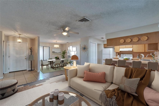 living area with light tile patterned floors, visible vents, ceiling fan with notable chandelier, and a textured ceiling