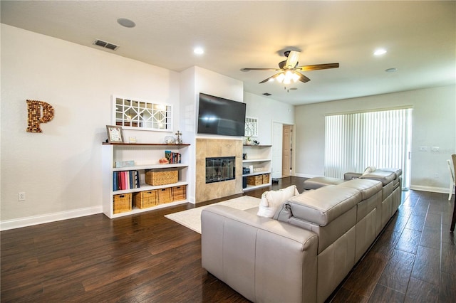 living area with visible vents, dark wood-type flooring, baseboards, ceiling fan, and a tile fireplace