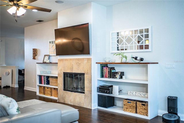 living area featuring visible vents, a ceiling fan, a tiled fireplace, wood finished floors, and baseboards