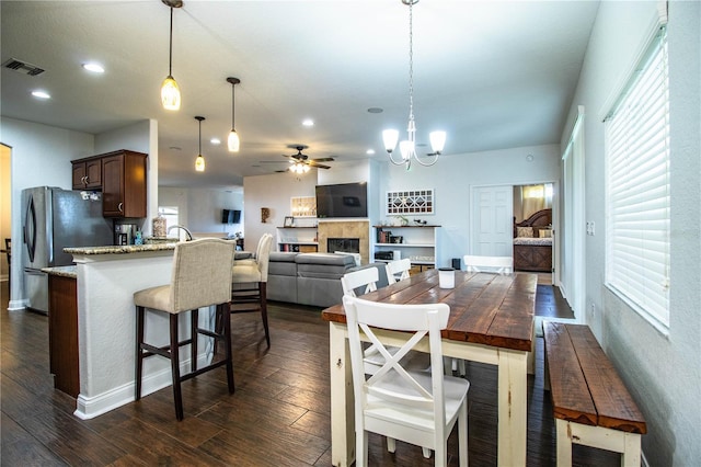 dining room with visible vents, dark wood finished floors, ceiling fan with notable chandelier, a fireplace, and recessed lighting