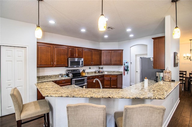 kitchen featuring light stone countertops, visible vents, a peninsula, dark wood-type flooring, and appliances with stainless steel finishes