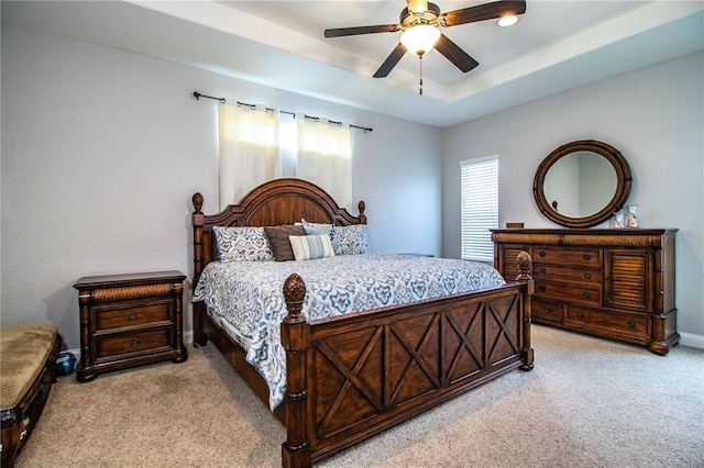 bedroom with light colored carpet, baseboards, a tray ceiling, and a ceiling fan