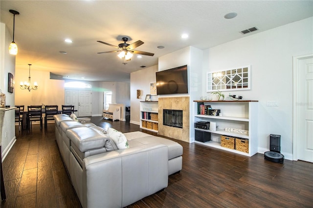 living room with visible vents, a tiled fireplace, ceiling fan with notable chandelier, dark wood-style floors, and baseboards