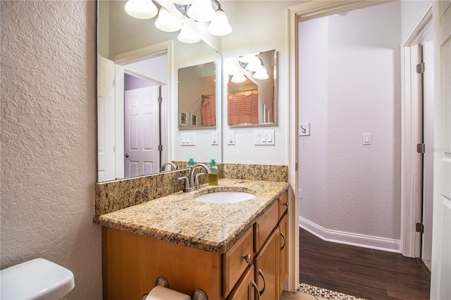 bathroom featuring vanity, wood finished floors, baseboards, toilet, and a textured wall