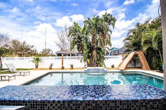 view of swimming pool featuring a fenced in pool, a water slide, a fenced backyard, and a patio area