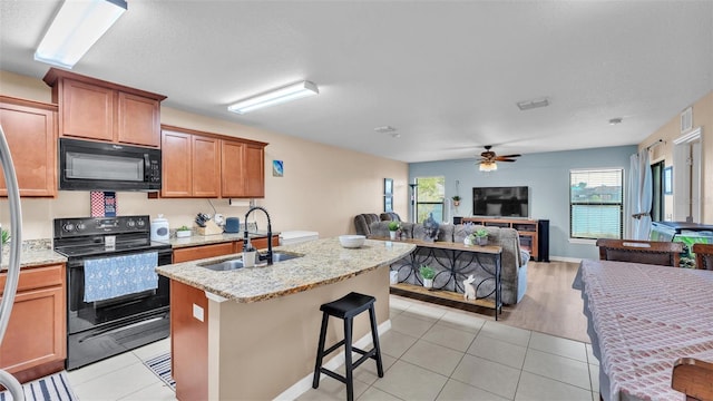 kitchen featuring black appliances, a kitchen island with sink, a sink, open floor plan, and light tile patterned floors