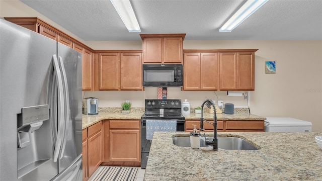 kitchen with a textured ceiling, black appliances, light stone counters, and a sink