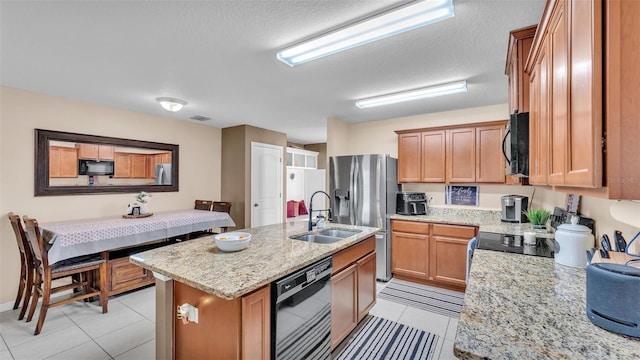 kitchen with light stone countertops, a center island with sink, light tile patterned flooring, black appliances, and a sink