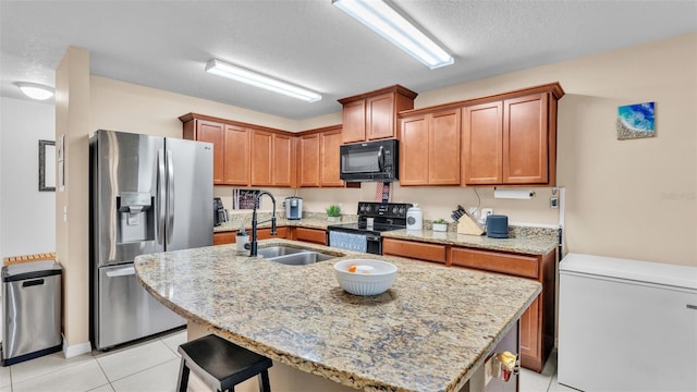 kitchen featuring light tile patterned floors, light stone countertops, an island with sink, a sink, and black appliances