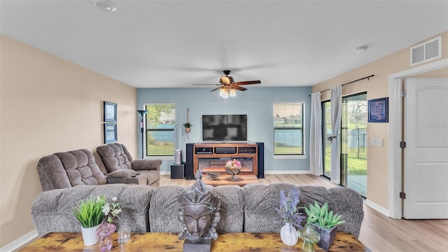 living area with a wealth of natural light, visible vents, light wood-style flooring, and baseboards