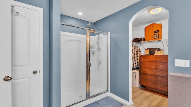 bathroom featuring a shower stall, wood finished floors, baseboards, and a textured ceiling