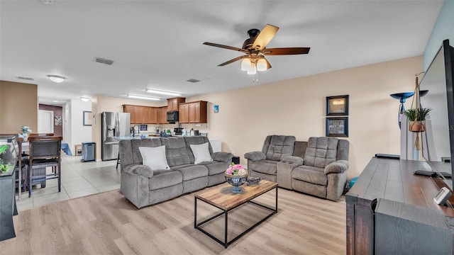 living room with visible vents, light wood-style flooring, and a ceiling fan