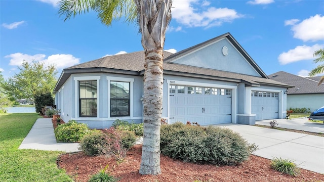 view of front of home with stucco siding, driveway, an attached garage, and a shingled roof