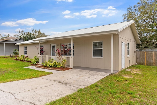 ranch-style house featuring metal roof, a porch, a front lawn, and fence