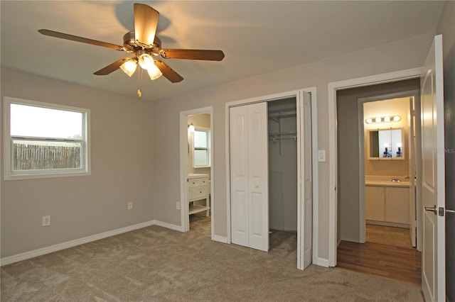 unfurnished bedroom with baseboards, carpet floors, a closet, ensuite bath, and a ceiling fan