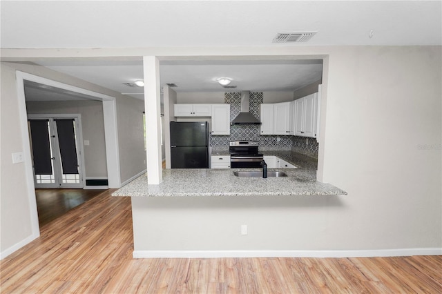 kitchen with stainless steel electric range oven, visible vents, a peninsula, freestanding refrigerator, and wall chimney exhaust hood