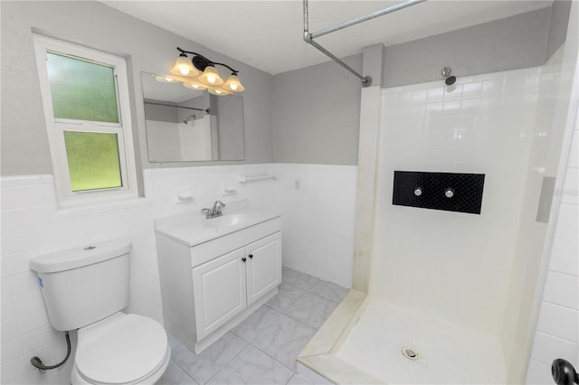 bathroom featuring a wainscoted wall, toilet, vanity, tiled shower, and tile walls