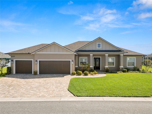 craftsman house with a front yard, roof with shingles, stucco siding, a garage, and decorative driveway