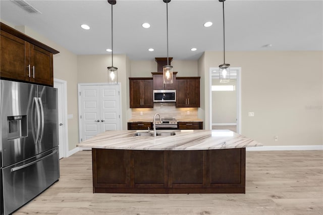 kitchen with light stone countertops, a sink, stainless steel appliances, dark brown cabinets, and tasteful backsplash