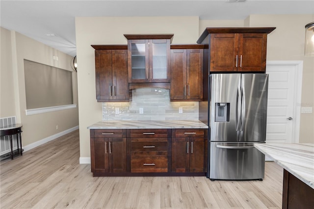 kitchen with light stone counters, glass insert cabinets, stainless steel fridge, light wood finished floors, and decorative backsplash