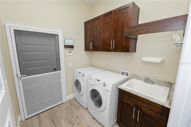 washroom with light wood-style flooring, a sink, cabinet space, baseboards, and washing machine and clothes dryer