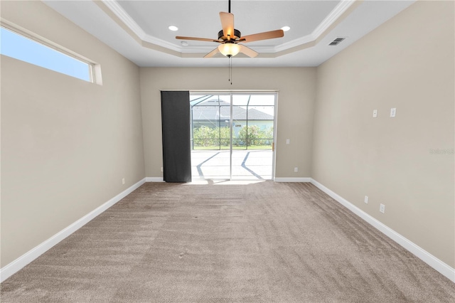 carpeted spare room featuring a tray ceiling, baseboards, visible vents, and ornamental molding