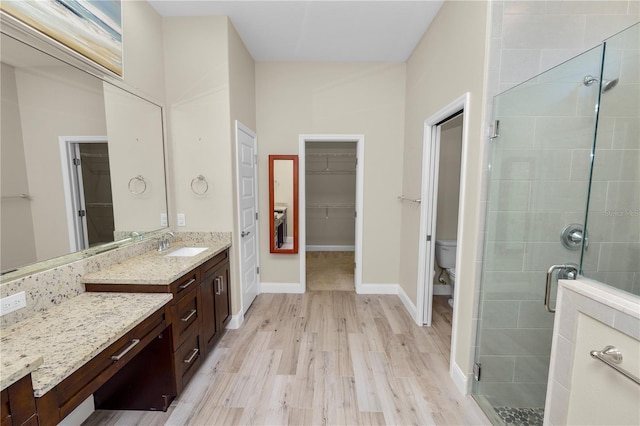 bathroom featuring toilet, a stall shower, wood finished floors, vanity, and a spacious closet