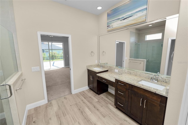 bathroom featuring a stall shower, wood finished floors, two vanities, and a sink