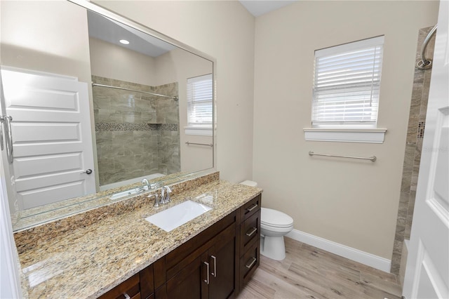 full bathroom featuring baseboards, toilet, a tile shower, wood finished floors, and vanity