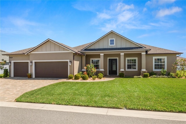 craftsman inspired home featuring stucco siding, decorative driveway, a front yard, a shingled roof, and a garage