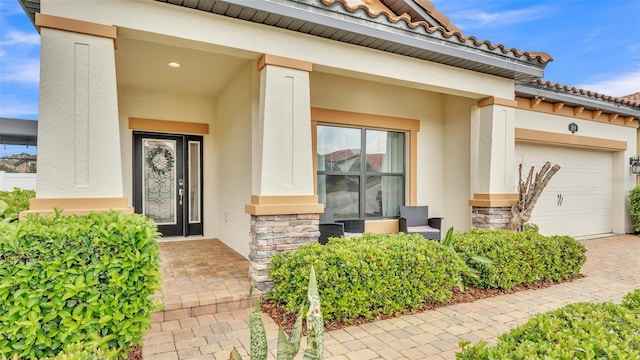 entrance to property with stone siding, stucco siding, a tiled roof, and an attached garage