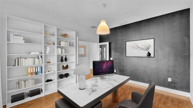 home office with visible vents, an accent wall, baseboards, and wood finished floors