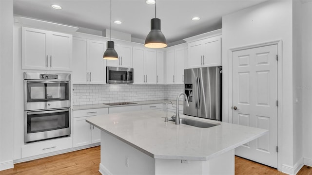 kitchen with a sink, decorative backsplash, white cabinets, appliances with stainless steel finishes, and light wood-type flooring