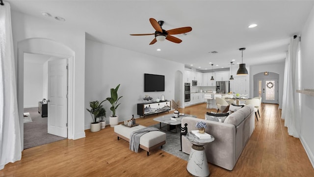 living area with recessed lighting, arched walkways, and light wood finished floors