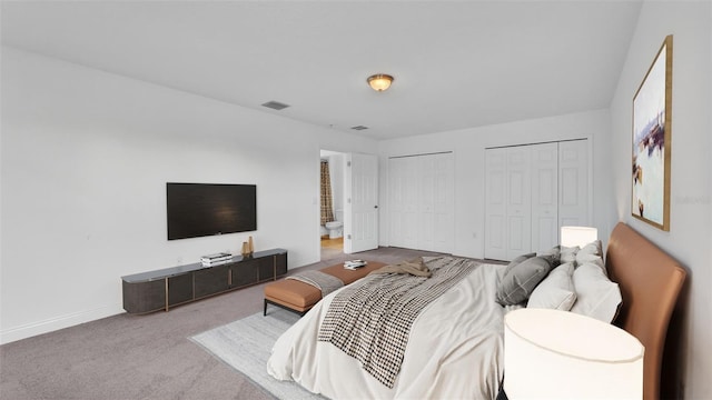 bedroom with carpet, visible vents, baseboards, ensuite bath, and multiple closets