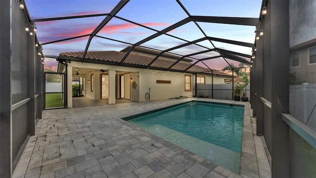 pool at dusk featuring glass enclosure, a patio, and a fenced in pool