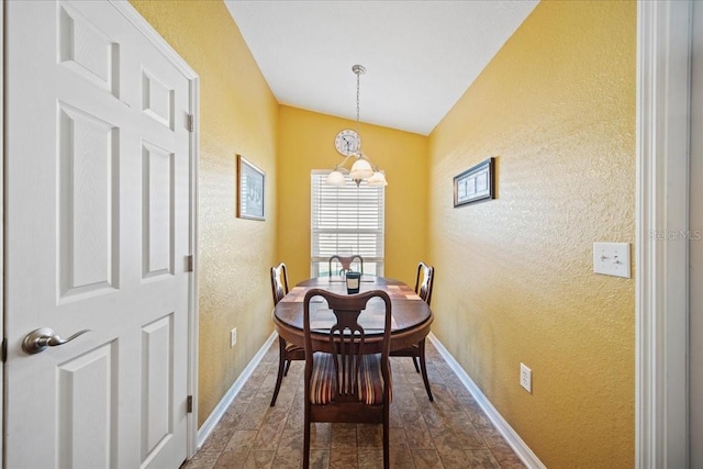 dining area with an inviting chandelier, a textured wall, and baseboards