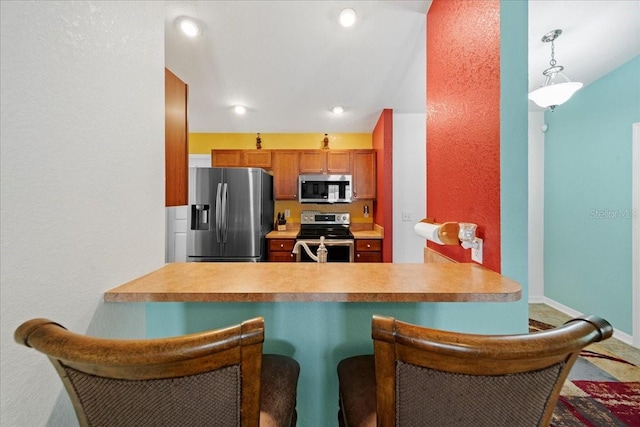 kitchen featuring a kitchen bar, stainless steel appliances, a peninsula, brown cabinetry, and baseboards