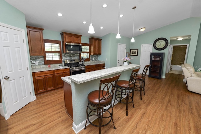 kitchen featuring light wood finished floors, a kitchen island, a breakfast bar, lofted ceiling, and appliances with stainless steel finishes