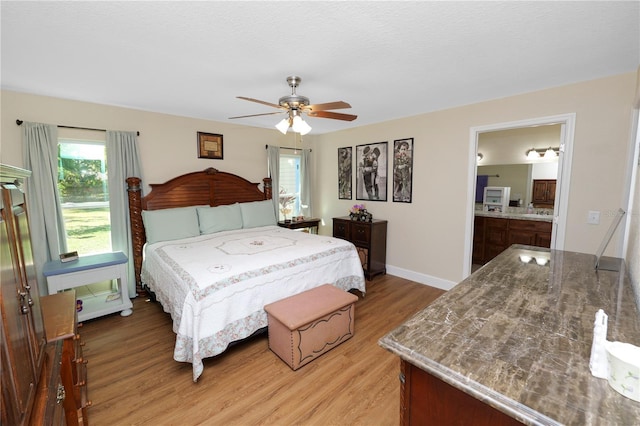 bedroom featuring ensuite bathroom, a ceiling fan, light wood-type flooring, and baseboards